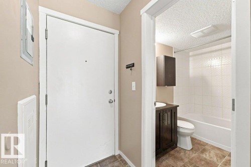 Entryway featuring a white door with a peephole, light beige walls, and brown tiled flooring - #119 111 Watt Cm Sw, Edmonton, AB - Indoor Photo Showing Bathroom