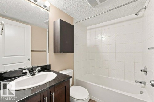 Bathroom featuring a white bathtub, white tiled shower surround, dark wood-finish vanity with an undermount sink, and a dark countertop - #119 111 Watt Cm Sw, Edmonton, AB - Indoor Photo Showing Bathroom
