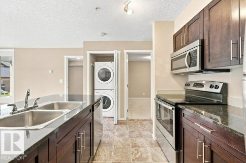 Kitchen featuring dark wood-finish cabinetry, stainless steel appliances, and a double basin sink - #119 111 Watt Cm Sw, Edmonton, AB - Indoor Photo Showing Kitchen With Double Sink