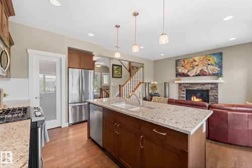 Open concept living space featuring a central kitchen island with a granite-style countertop and integrated sink - 3413 Cameron Heights Cove Nw, Edmonton, AB - Indoor Photo Showing Kitchen With Fireplace With Upgraded Kitchen