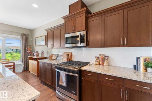Well-appointed kitchen featuring granite countertops, full-height wood cabinetry, stainless steel appliances, a subway tile backsplash, and wood-finish flooring - 3413 Cameron Heights Cove Nw, Edmonton, AB - Indoor Photo Showing Kitchen