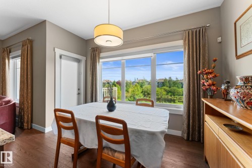 Dining area featuring wood-finish flooring, a contemporary drum pendant light, and a prominent window array with a verdant exterior outlook - 3413 Cameron Heights Cove Nw, Edmonton, AB - Indoor Photo Showing Dining Room
