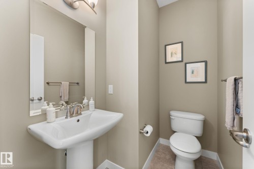 Powder room featuring a pedestal sink with brushed nickel faucet, large wall mirror, and tile flooring - 3413 Cameron Heights Cove Nw, Edmonton, AB - Indoor Photo Showing Bathroom