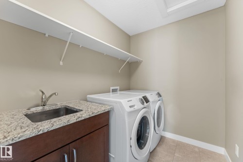 Laundry area featuring a utility sink with a stainless steel faucet, a granite-finish countertop, and dark wood-finish cabinetry - 3413 Cameron Heights Cove Nw, Edmonton, AB - Indoor Photo Showing Laundry Room