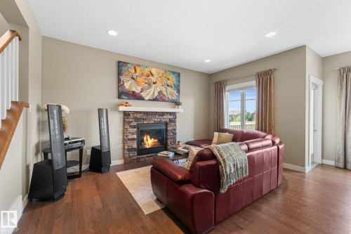 Living space featuring a stone-faced fireplace with a wood mantel, wood-finish flooring, and recessed lighting - 3413 Cameron Heights Cove Nw, Edmonton, AB - Indoor Photo Showing Living Room With Fireplace