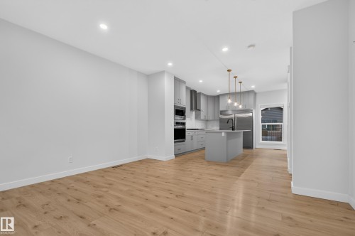 Open-concept living space featuring wood-finish flooring, a modern kitchen island with a black faucet, light gray cabinetry, stainless steel appliances, and recessed lighting - 1534 Plum Circle Circle Sw, Edmonton, AB - Indoor Photo Showing Kitchen
