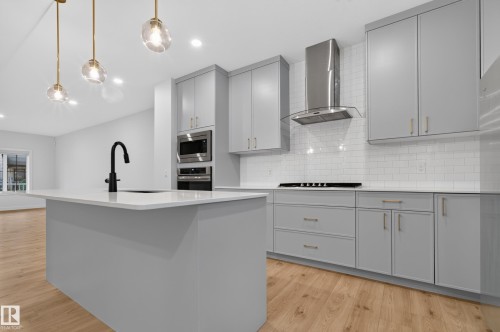 Kitchen featuring light gray cabinetry, a central island with a sink and matte black faucet, and light wood-finish flooring - 1534 Plum Circle Circle Sw, Edmonton, AB - Indoor Photo Showing Kitchen