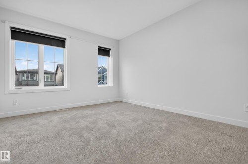 Spacious room featuring light gray carpet, white walls, and two windows with white trim and black roller shades - 1534 Plum Circle Circle Sw, Edmonton, AB - Indoor Photo Showing Other Room