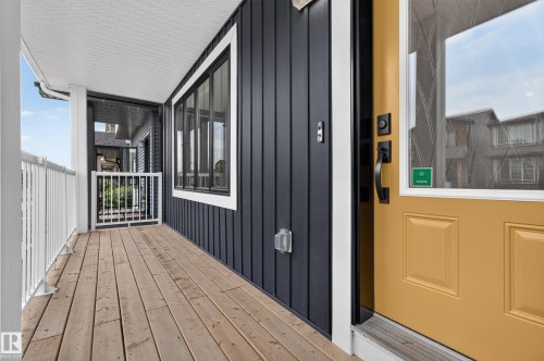 Inviting front porch featuring a mustard yellow front door with decorative glass, a horizontal wood-plank deck, and white railings - 1534 Plum Circle Circle Sw, Edmonton, AB - Outdoor With Exterior