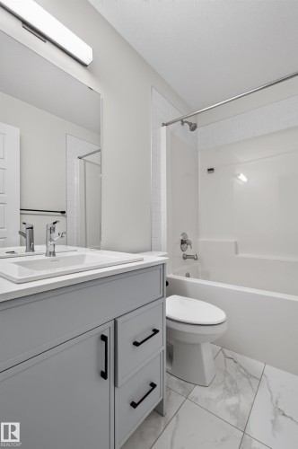 Bathroom featuring a light gray vanity with a white countertop and integrated sink, chrome faucet, rectangular mirror, and overhead linear light fixture - 1534 Plum Circle Circle Sw, Edmonton, AB - Indoor Photo Showing Bathroom