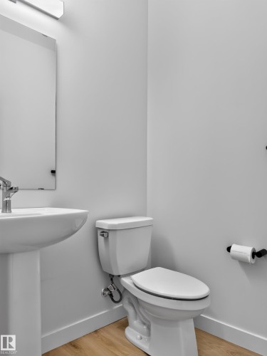 Pedestal sink with chrome faucet, toilet with white baseboard trim, and wood-finish flooring - 1534 Plum Circle Circle Sw, Edmonton, AB - Indoor Photo Showing Bathroom