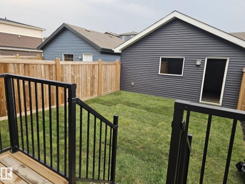 Expansive grassy backyard featuring a new privacy fence, a detached structure with horizontal siding, and a wooden deck with black metal railings - 1534 Plum Circle Circle Sw, Edmonton, AB - Outdoor With Exterior