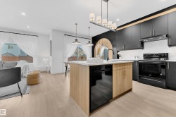 Modern kitchen featuring dark cabinetry, light wood-finish flooring, a central island with a light countertop, and a contemporary linear chandelier - 