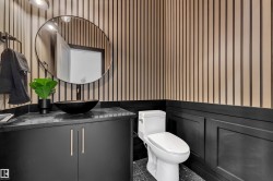 Contemporary powder room featuring a black vessel sink, dark cabinetry with bar pulls, and a circular mirror - 