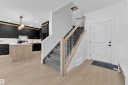 Contemporary kitchen featuring black cabinetry, light wood-finish flooring, a central island with integrated storage, and a staircase with light wood handrails and carpeted treads - 
