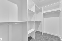 Walk-in closet featuring white built-in shelving, multiple hanging rods, and gray carpet flooring - 