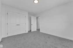 Crisp white walls define this room, featuring light gray carpeting and a flush-mount ceiling light fixture - 