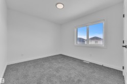 White walls complement gray carpeting in this room featuring a window with white trim, a flush-mount ceiling light, and a white door with black hardware - 