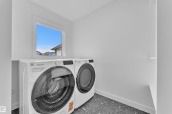 Dedicated laundry space featuring a window, light-toned walls, and dark speckled flooring - 