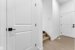 Interior hallway featuring white paneled doors with matte black hardware, wood-finish flooring, and a staircase with wood-finish treads - 