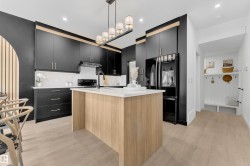 Contemporary kitchen featuring black cabinetry, light wood-finish flooring, a central island with a white countertop, and integrated appliances - 