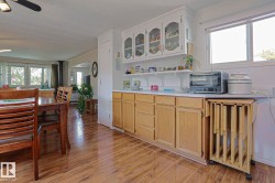 Kitchen area featuring wood-finish flooring, light-toned base cabinetry, and white upper cabinets with glass-paneled doors - 
