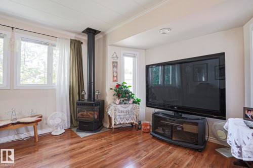 Living area featuring wood-finish flooring, a freestanding stove fireplace with a black flue, and multiple windows providing natural illumination - 137 Lee Ridge Road Nw, Edmonton, AB - Indoor