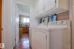 Dedicated laundry area featuring white upper cabinetry, a built-in shelf, and wood-finish flooring - 