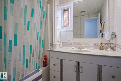 Bathroom featuring a built-in tub with a white tile surround, a single vanity with an integrated sink, a large mirror, and a frosted glass window - 137 Lee Ridge Road Nw, Edmonton, AB - Indoor Photo Showing Bathroom