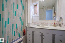 Bathroom featuring a built-in tub with a white tile surround, a single vanity with an integrated sink, a large mirror, and a frosted glass window - 