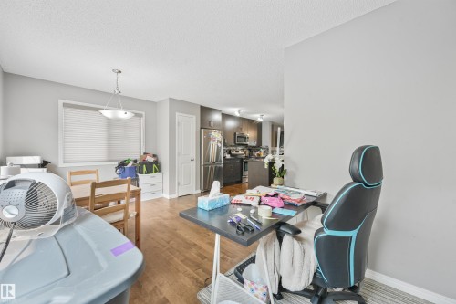 Open-concept living area featuring wood-finish flooring, a contemporary ceiling light fixture, and a window with blinds - #40 1030 Chappelle Bv Sw, Edmonton, AB - Indoor