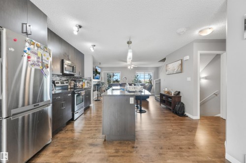 Open-concept kitchen featuring dark wood-finish cabinetry, stainless steel appliances, and a central island with a breakfast bar - #40 1030 Chappelle Bv Sw, Edmonton, AB - Indoor Photo Showing Kitchen With Stainless Steel Kitchen With Upgraded Kitchen