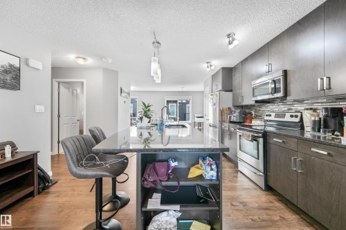 Kitchen featuring a dark stone countertop island with integrated shelving, stainless steel appliances, and wood-finish flooring - #40 1030 Chappelle Bv Sw, Edmonton, AB - Indoor Photo Showing Kitchen With Upgraded Kitchen