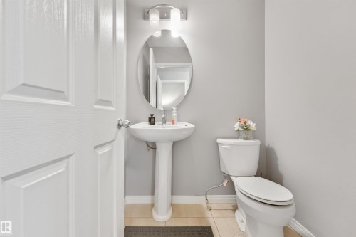 Powder room featuring a white pedestal sink, oval mirror, and contemporary wall sconce - #40 1030 Chappelle Bv Sw, Edmonton, AB - Indoor Photo Showing Bathroom