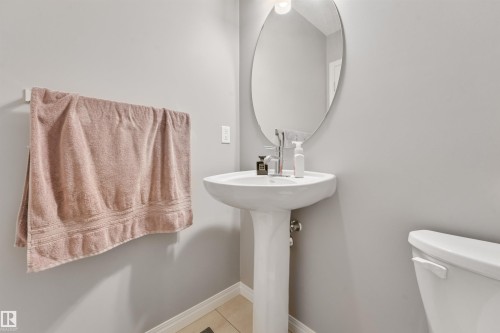 Pedestal sink with an oval mirror and contemporary wall sconce - #40 1030 Chappelle Bv Sw, Edmonton, AB - Indoor Photo Showing Bathroom