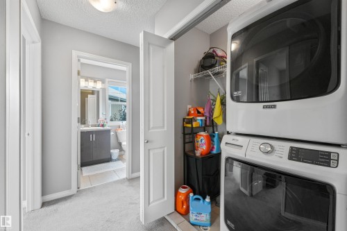 Dedicated laundry area featuring a stacked washer and dryer, an overhead wire shelving unit, and tile flooring - #40 1030 Chappelle Bv Sw, Edmonton, AB - Indoor Photo Showing Laundry Room