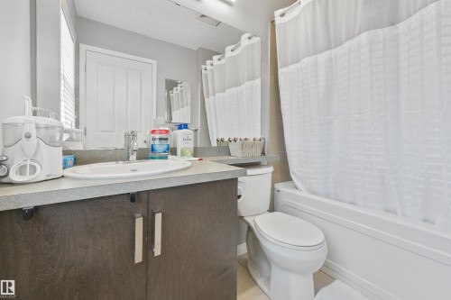 Bathroom featuring a single vanity with an integrated sink, a dark wood-finish cabinet with silver-tone hardware, a light-toned countertop, and a built-in tub with a shower - #40 1030 Chappelle Bv Sw, Edmonton, AB - Indoor Photo Showing Bathroom