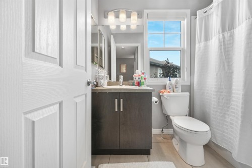 Bathroom featuring a wood-finish vanity with a light-toned countertop, a rectangular window with grilles, and light-toned tile flooring - #40 1030 Chappelle Bv Sw, Edmonton, AB - Indoor Photo Showing Bathroom