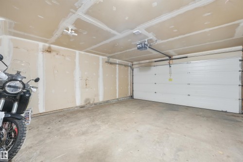 Attached garage featuring a concrete floor, an overhead door with opener, and exposed drywall - #40 1030 Chappelle Bv Sw, Edmonton, AB - Indoor Photo Showing Garage