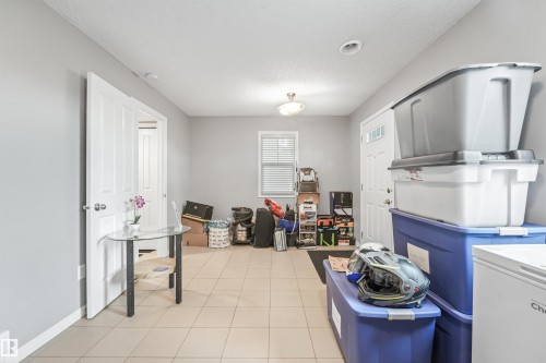 Light beige tiled flooring extending through the space, light gray painted walls, a white paneled interior door, and a white exterior door with glass inserts - #40 1030 Chappelle Bv Sw, Edmonton, AB - Indoor With Fireplace