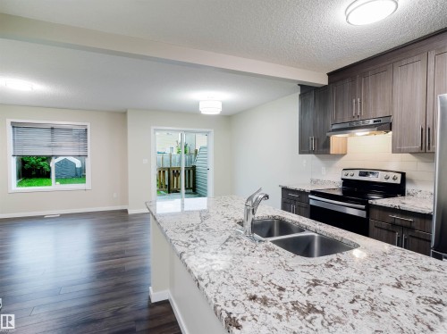 Kitchen featuring a large island with a double stainless steel sink and granite countertop, dark wood-finish cabinetry, a subway tile backsplash, and stainless steel appliances - 5407 14 Avenue Sw, Edmonton, AB - Indoor Photo Showing Kitchen With Stainless Steel Kitchen With Double Sink With Upgraded Kitchen