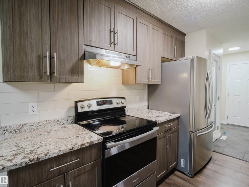 Kitchen featuring wood-finish cabinetry, granite-style countertops, white subway tile backsplash, stainless steel appliances, and wood-finish flooring - 5407 14 Avenue Sw, Edmonton, AB - Indoor Photo Showing Kitchen With Stainless Steel Kitchen With Upgraded Kitchen