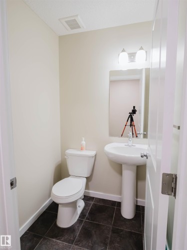 Bathroom featuring dark-toned tile flooring, a white pedestal sink, and a matching white toilet - 5407 14 Avenue Sw, Edmonton, AB - Indoor Photo Showing Bathroom