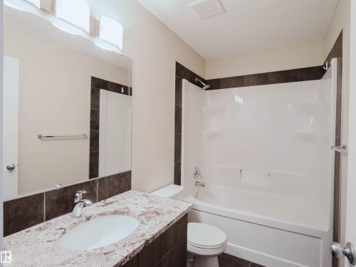 Bathroom featuring a white integrated tub and shower unit, dark tile surround, and a vanity with a light-colored speckled countertop - 5407 14 Avenue Sw, Edmonton, AB - Indoor Photo Showing Bathroom