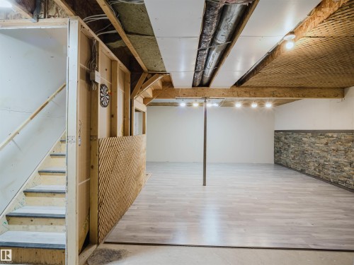 Spacious unfinished lower level featuring wood-finish flooring, a partial stone accent wall, recessed lighting, and an exposed wood beam ceiling - 5407 14 Avenue Sw, Edmonton, AB - Indoor