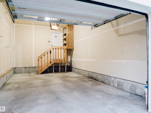 Spacious garage with concrete flooring, natural wood staircase and railing, built-in shelving, and exposed joists - 5407 14 Avenue Sw, Edmonton, AB - Indoor Photo Showing Garage