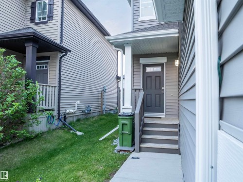 Front entry featuring a dark gray paneled door with glass inserts, wood-finish steps with railings, and a covered porch - 5407 14 Avenue Sw, Edmonton, AB - Outdoor