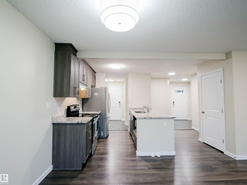Modern kitchen featuring dark wood-finish cabinetry, light-toned granite countertops, a stainless steel appliance suite, and a spacious island with an undermount sink - 5407 14 Avenue Sw, Edmonton, AB - Indoor Photo Showing Kitchen