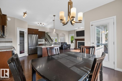 Dining area featuring a contemporary chandelier, wood-finish flooring, and a glass-paneled exterior door - 109 Selkirk Place, Leduc, AB - Indoor Photo Showing Dining Room