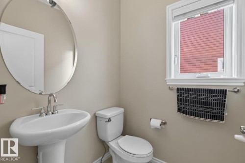 Pedestal sink with chrome faucet, oval mirror, and a window with white trim - 109 Selkirk Place, Leduc, AB - Indoor Photo Showing Bathroom